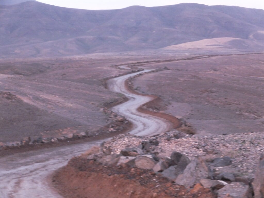 Dusty path winding through desert type landscape with hillsin distance