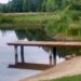 wooden walkway to lake forest in background grass in front sky above